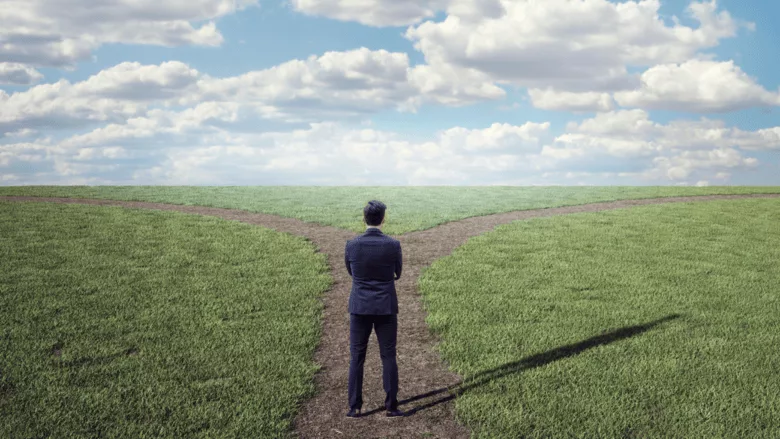 A man in a business suit stands at a fork in the road.