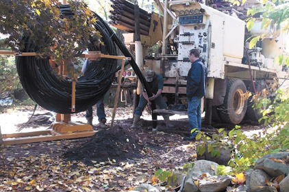 Drillers with Colaluce Well & Pump Service feed Twister piping from a reel into a borehole at a jobsite in New Jersey.